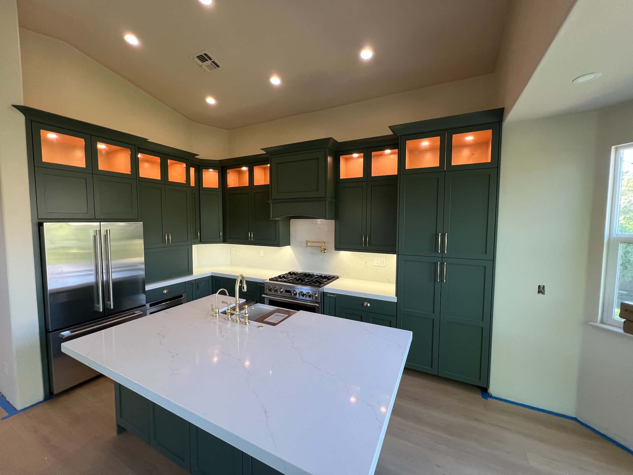 Deep green custom kitchen cabinetry with lit upper cabinets