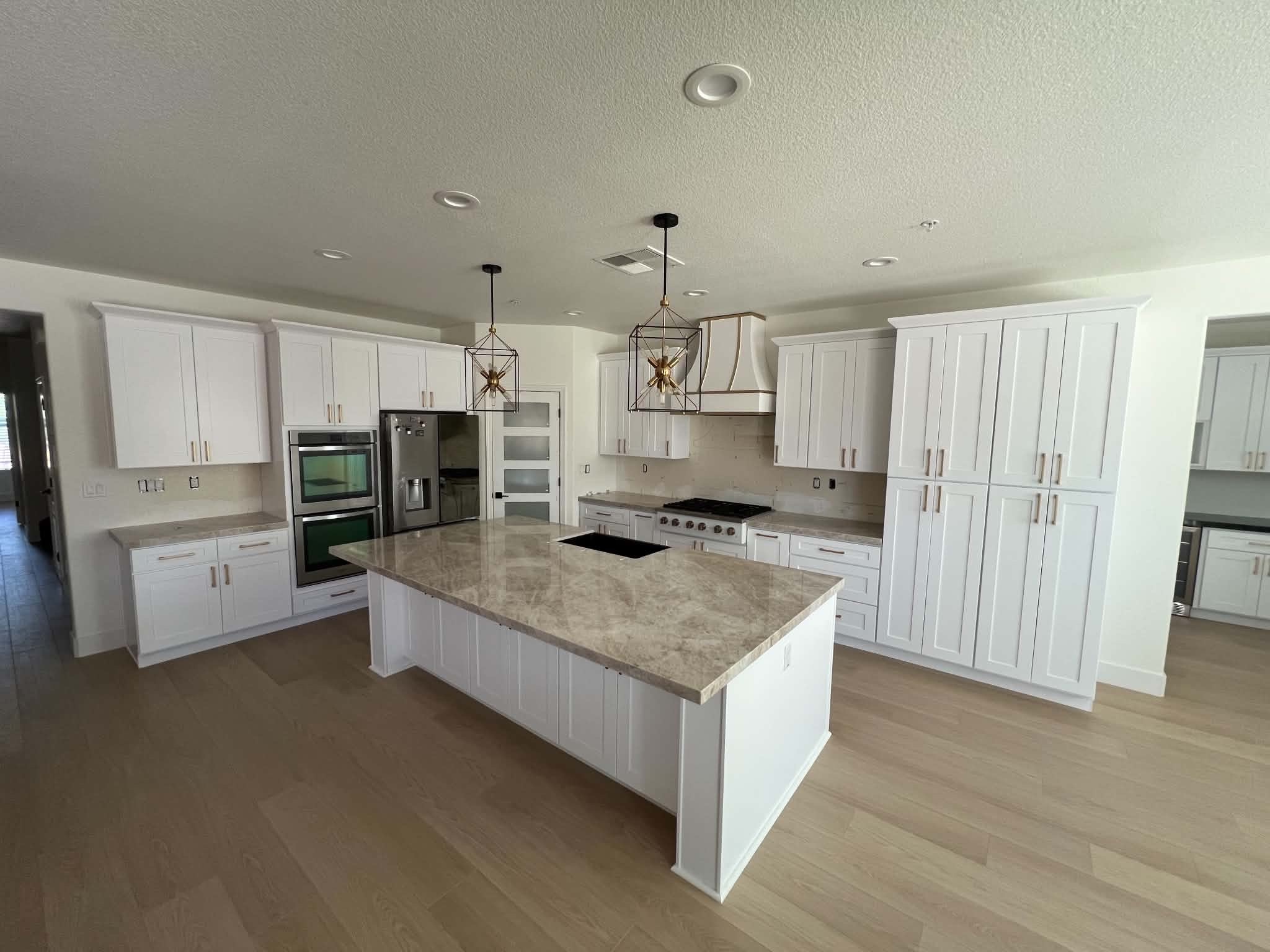 Finished white custom kitchen with statement range hood, full-height cabinetry and central island